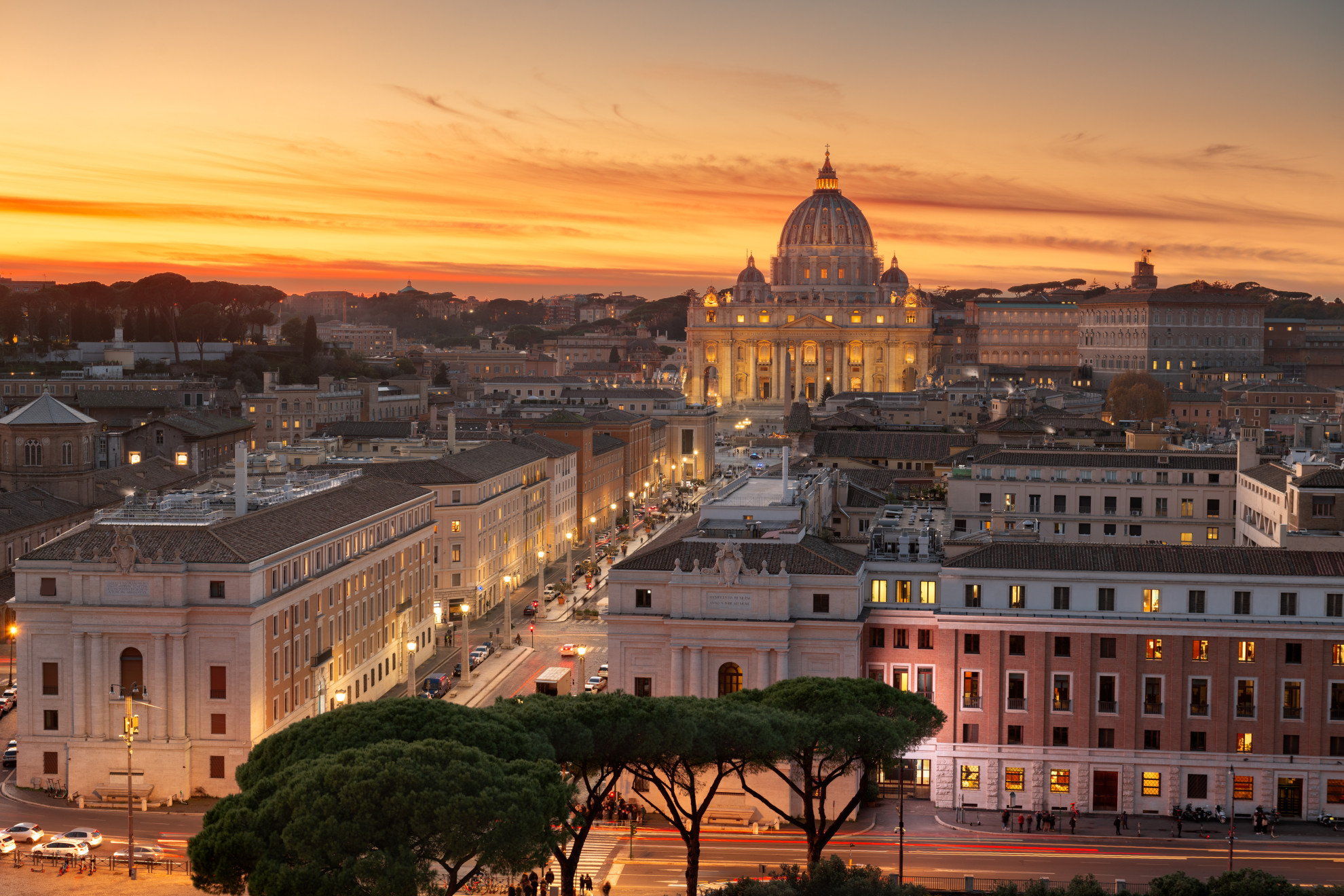 Illuminated St Peter's Basilica at sunset with Via della Conciliazione and Rome's rooftops in the foreground, Vatican City, Italy