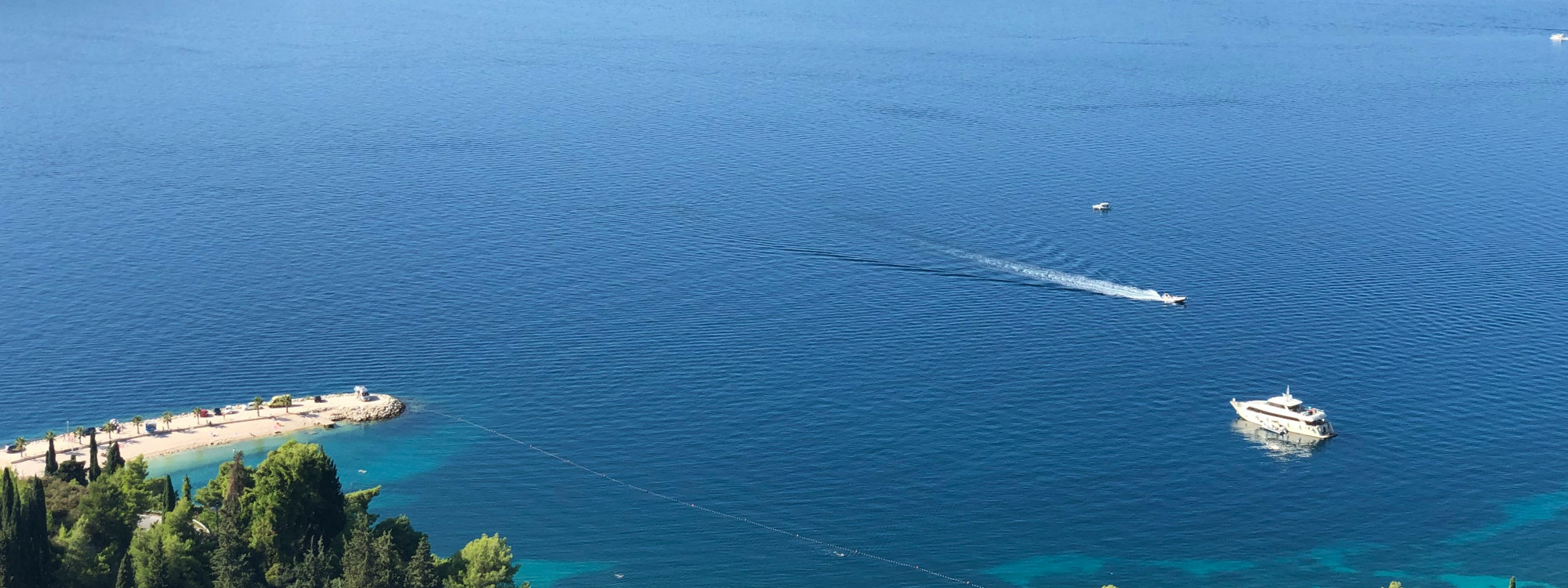 Cruise ship sailing across the deep blue Adriatic Sea near Dubrovnik, Croatia, leaving gentle wakes across the water beside the Dalmatian coastline.