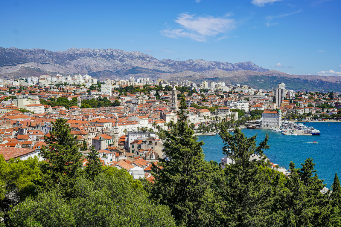 : Panoramic view across Split, Croatia, with terracotta rooftops, the historic centre and waterfront framed by the mountains of the Dalmatian coast.