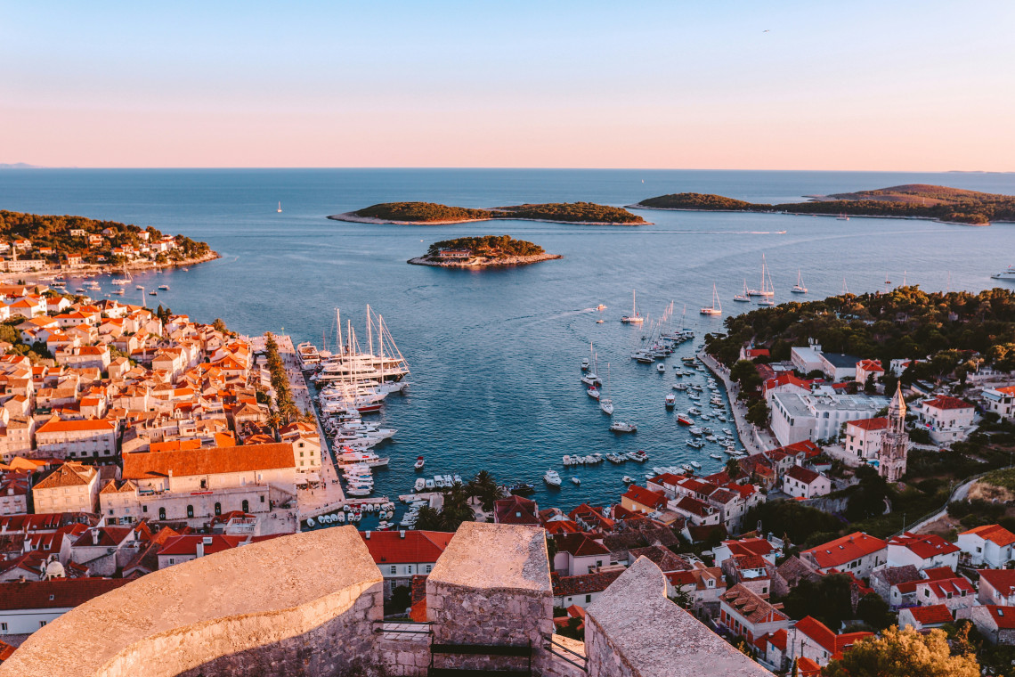 Elevated sunset view over Hvar Town in Croatia, with its marina, terracotta rooftops and boats overlooking the Pakleni Islands in the Adriatic Sea.