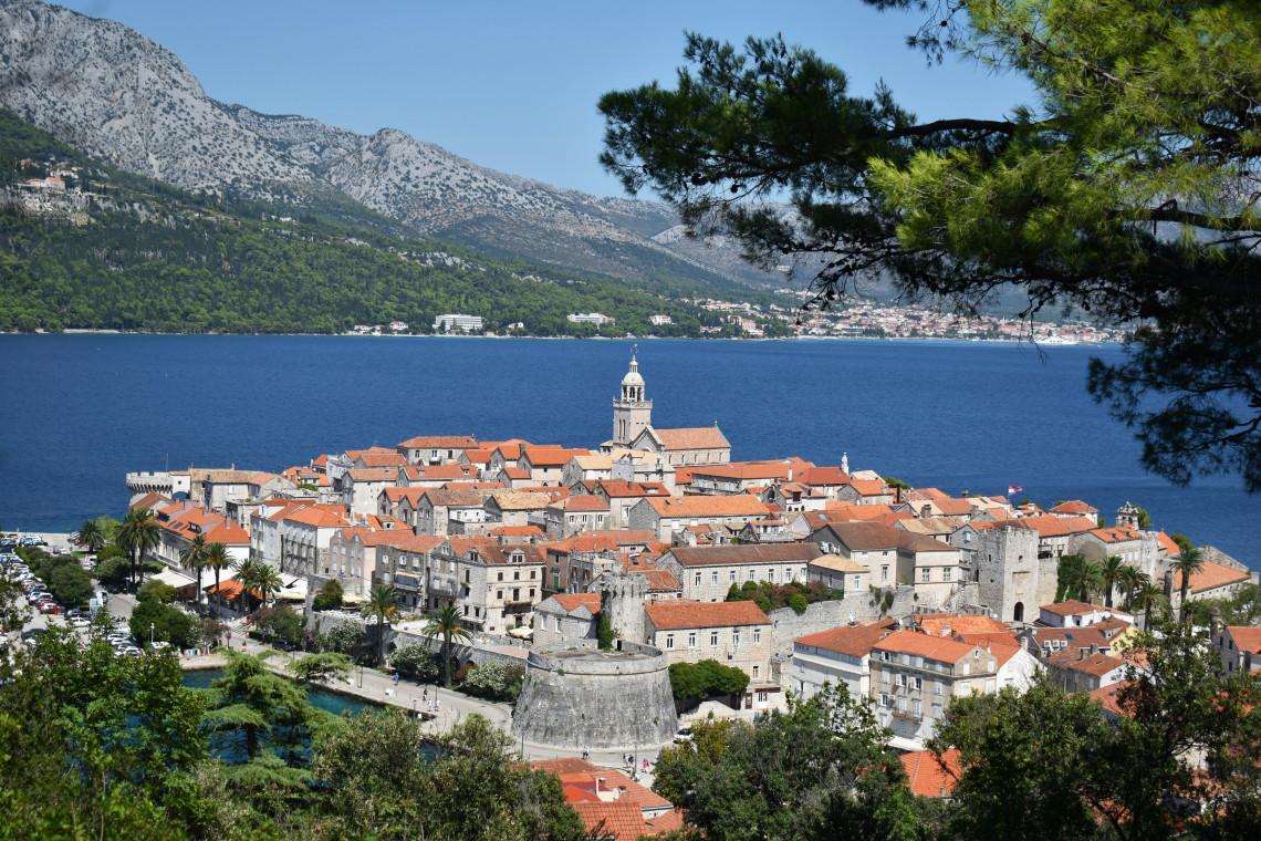 Korčula Old Town in Croatia occupies a compact peninsula surrounded by blue Adriatic waters, with medieval stone buildings, defensive walls and terracotta rooftops backed by mountains.