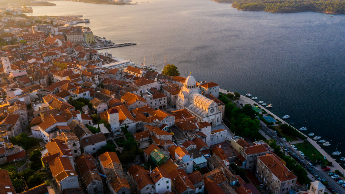 Aerial view across &Scaron;ibenik, Croatia, with dense terracotta rooftops, historic stone buildings and the Cathedral of St James beside the Adriatic waterfront in warm evening light.