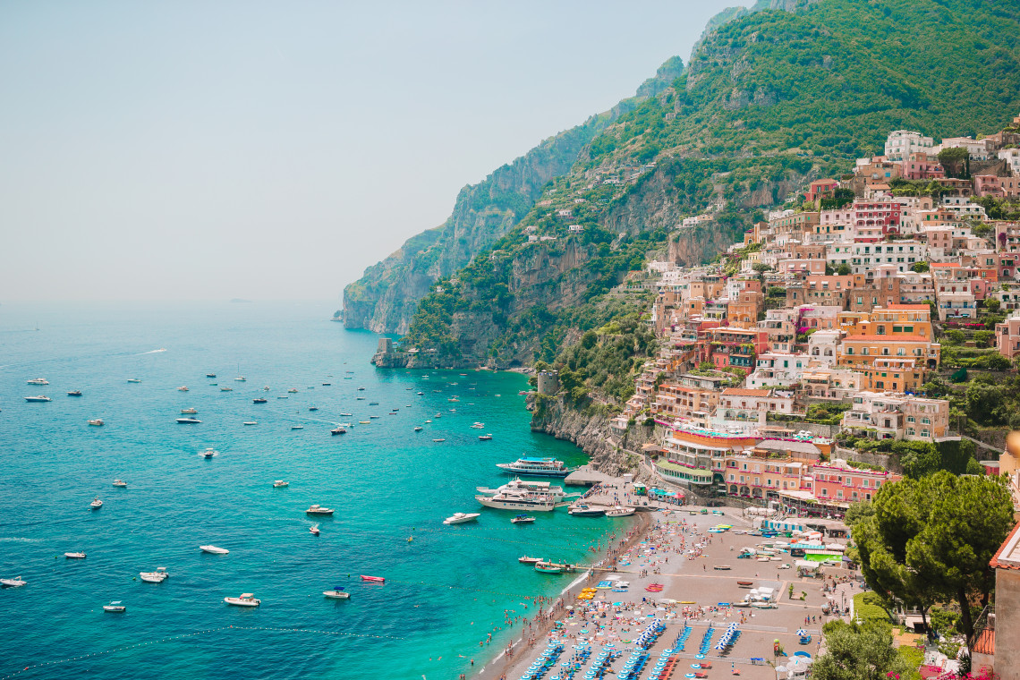 Positano rises steeply above Marina Grande Beach on the Amalfi Coast in Italy. Colourful buildings cover the rocky hillside while boats dot the turquoise Mediterranean waters below.