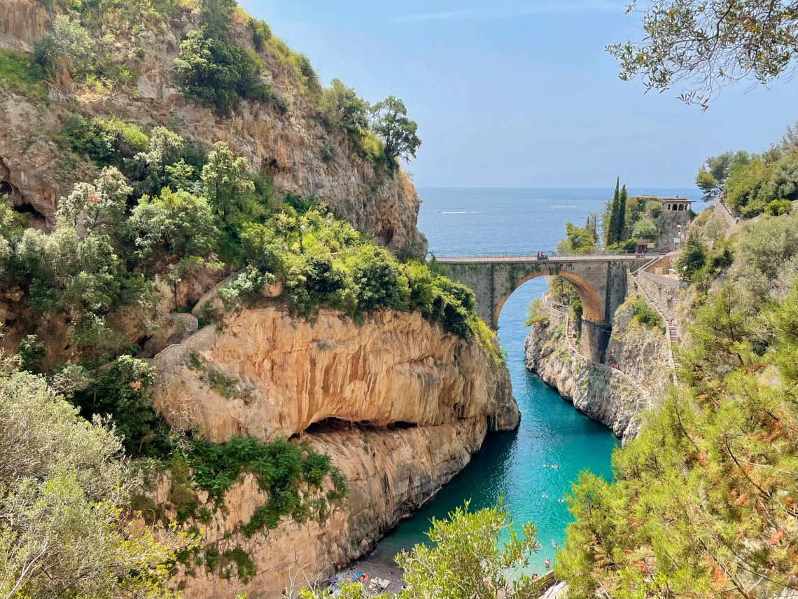 Fiordo di Furore cuts through steep limestone cliffs on Italy&rsquo;s Amalfi Coast, with a stone bridge spanning the narrow inlet. Clear turquoise water fills the sheltered cove beneath the rocky slopes and Mediterranean vegetation.