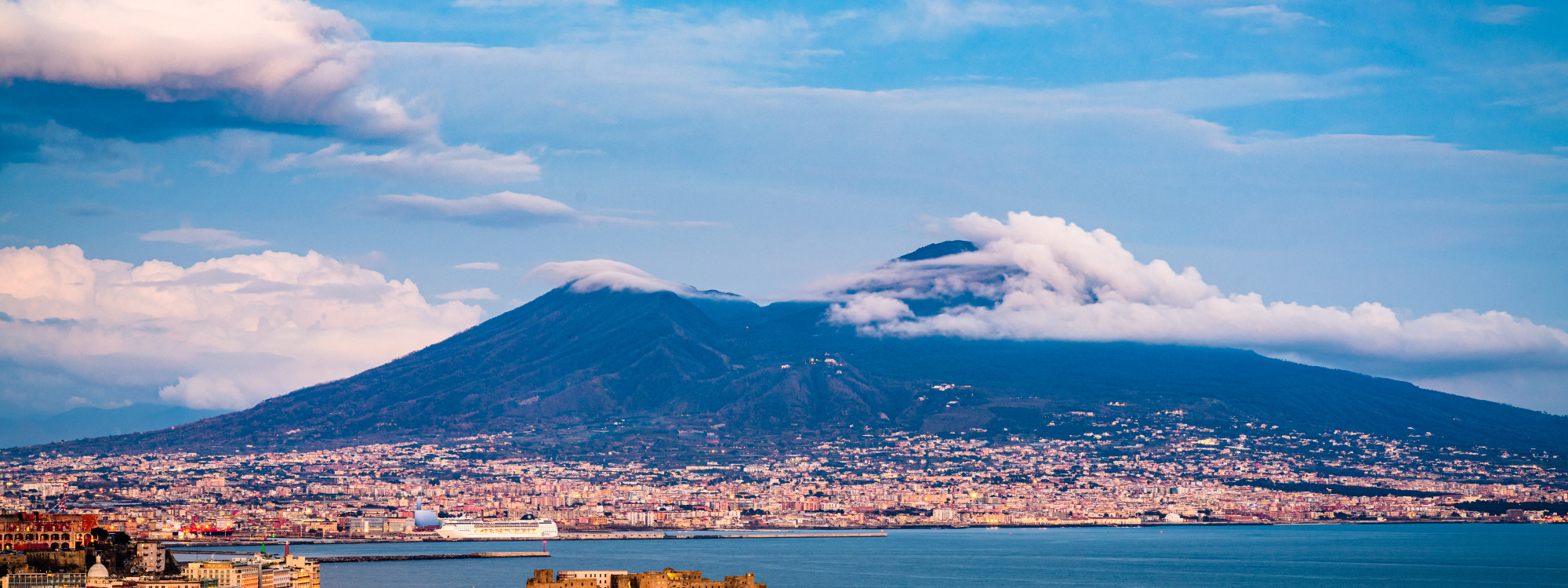 Panoramic view of Mount Vesuvius volcano rising above the sprawling city of Naples and the Bay of Naples under a dramatic cloudy sky, Campania, Italy