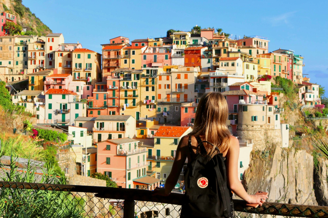 A traveller looks across the colourful houses of Manarola in Cinque Terre, Italy. The tightly packed buildings rise above steep rocky cliffs along the Ligurian coast.