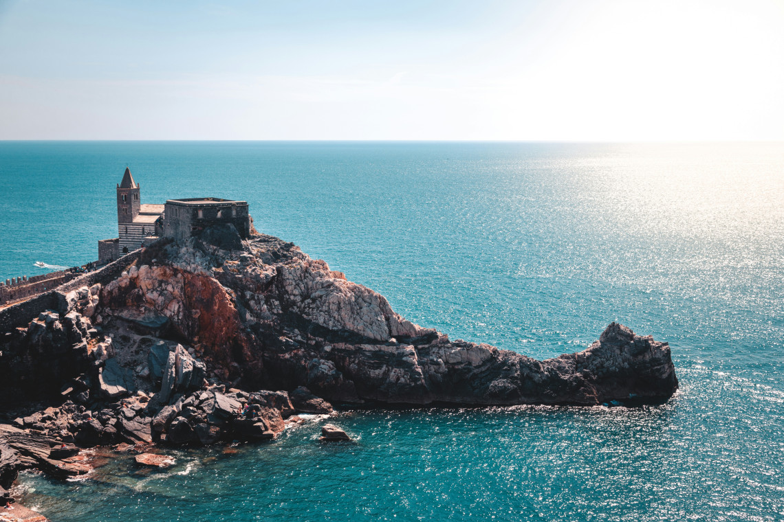 The Church of San Pietro stands on a rocky promontory overlooking the Ligurian Sea in Porto Venere, Italy. The historic stone church occupies the edge of the coastline surrounded by open Mediterranean water.