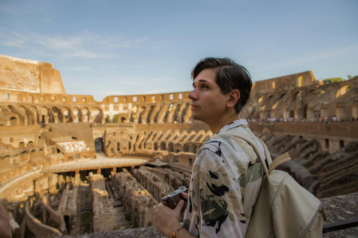 A visitor looks across the interior of the Colosseum in Rome, Italy. Ancient arches, seating levels and the exposed underground structures of the arena extend behind him.