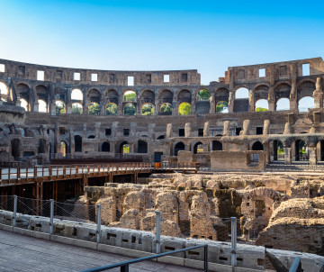 Interior view of the Colosseum in Rome, Italy, showing the ancient seating levels, stone arches and exposed underground hypogeum. The archaeological remains reveal the scale and construction of the Roman amphitheatre.
