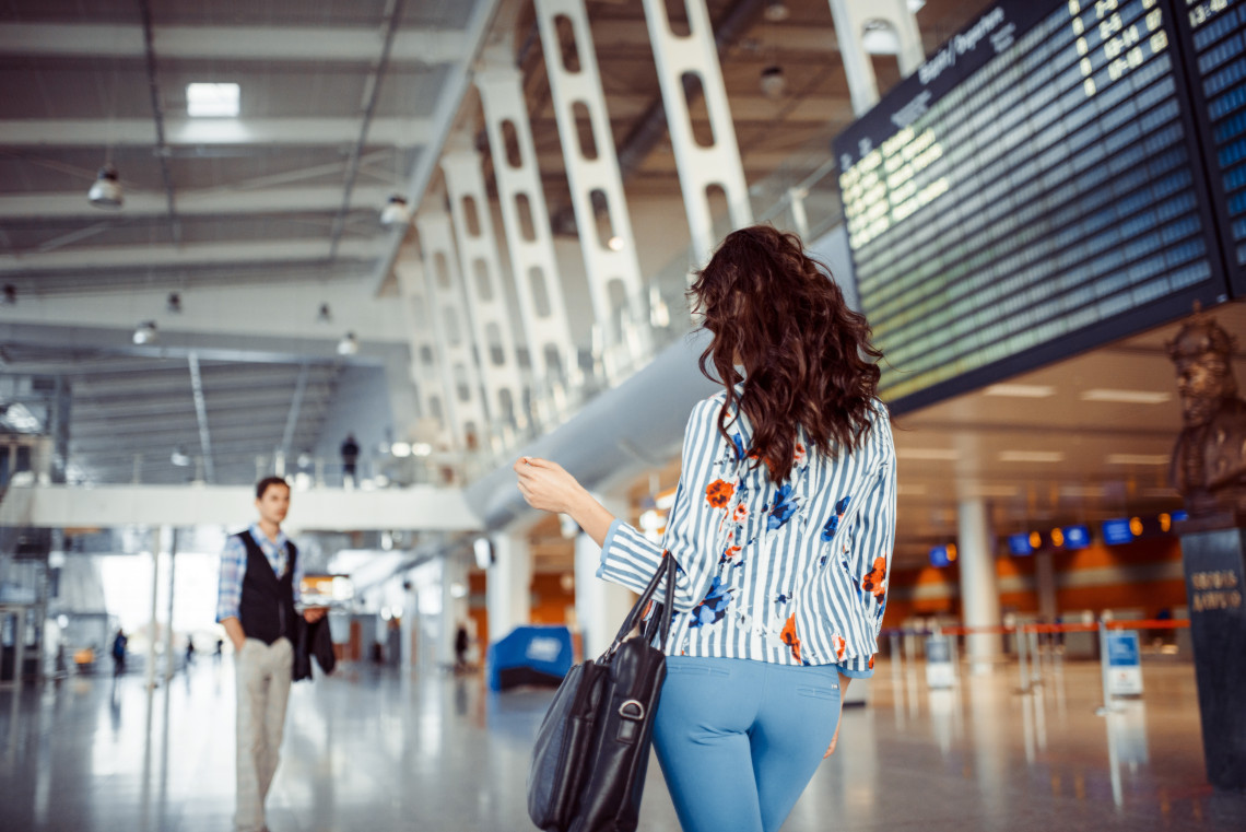 Woman with handbag checking flight departures board at an international airport terminal, traveling to Europe