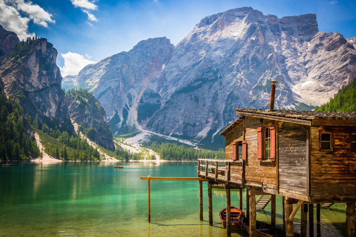 Historic wooden boathouse on stilts at the edge of Lago di Braies with turquoise glacial water and dramatic Dolomite peaks in the background, South Tyrol, Italy