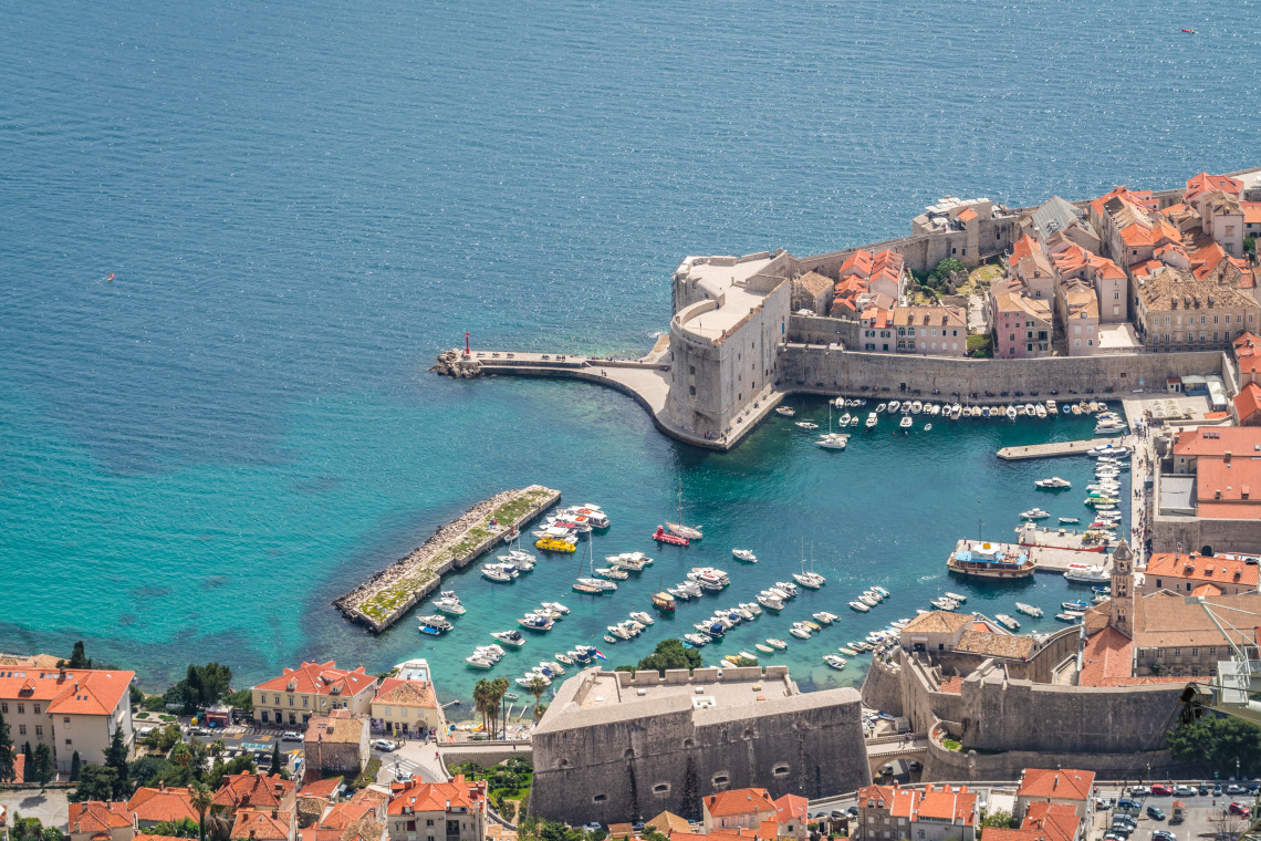 Elevated view of Dubrovnik&rsquo;s Old Port in Croatia, with small boats moored in turquoise Adriatic waters beneath the fortified stone walls and terracotta rooftops of the historic city.