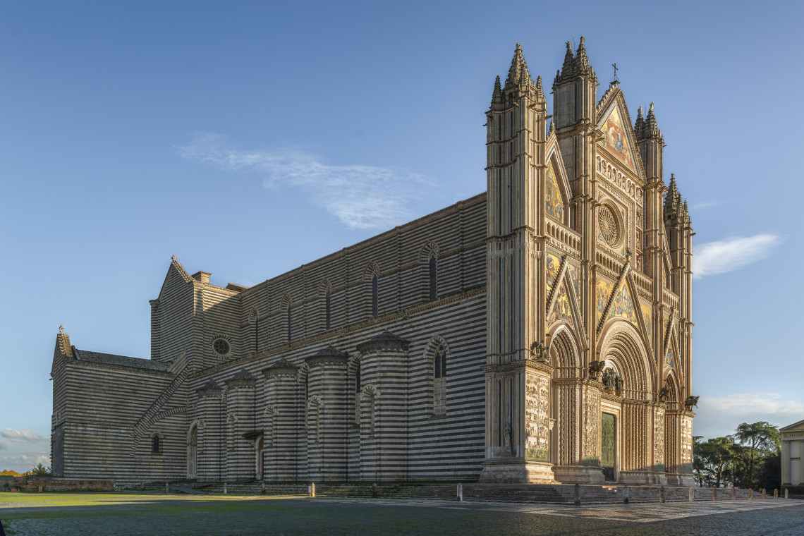 Orvieto Cathedral stands in the historic centre of Orvieto, Umbria, Italy, with its elaborate Gothic fa&ccedil;ade and alternating bands of light and dark stone along the exterior walls.