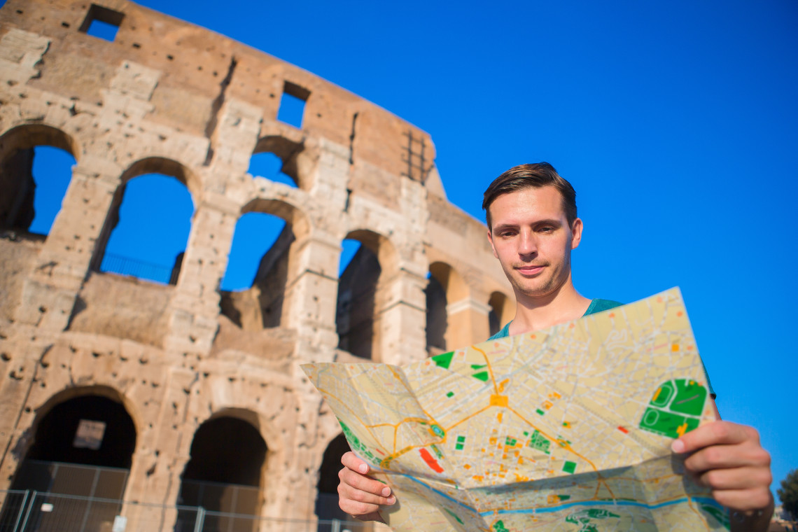 Young male tourist holding a map in front of the Colosseum in Rome, Italy