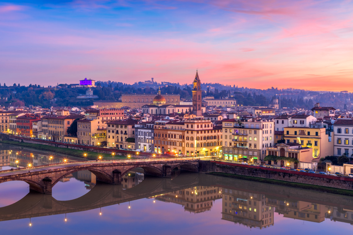Panoramic dusk view of Florence skyline with Ponte Santa Trinita reflected in the Arno River and illuminated buildings along the waterfront, Tuscany, Italy