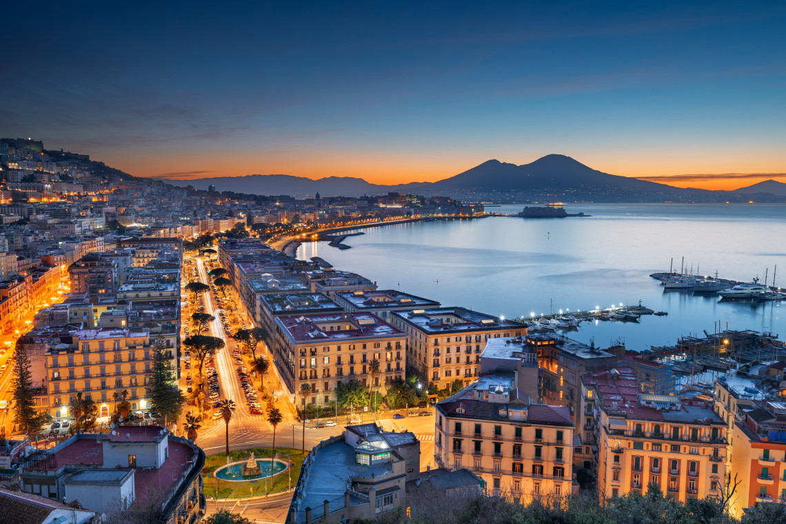 Aerial sunset view of Naples waterfront boulevard with city lights reflected on the Bay of Naples and Mount Vesuvius silhouetted in the background, Campania, Italy