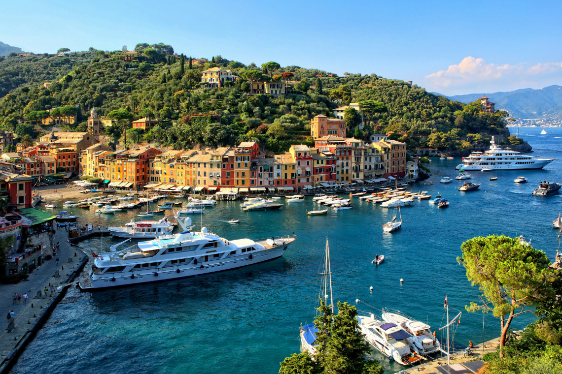 Aerial view of Portofino harbor with luxury yachts and colorful waterfront buildings nestled among forested hills on the Italian Riviera, Liguria, Italy
