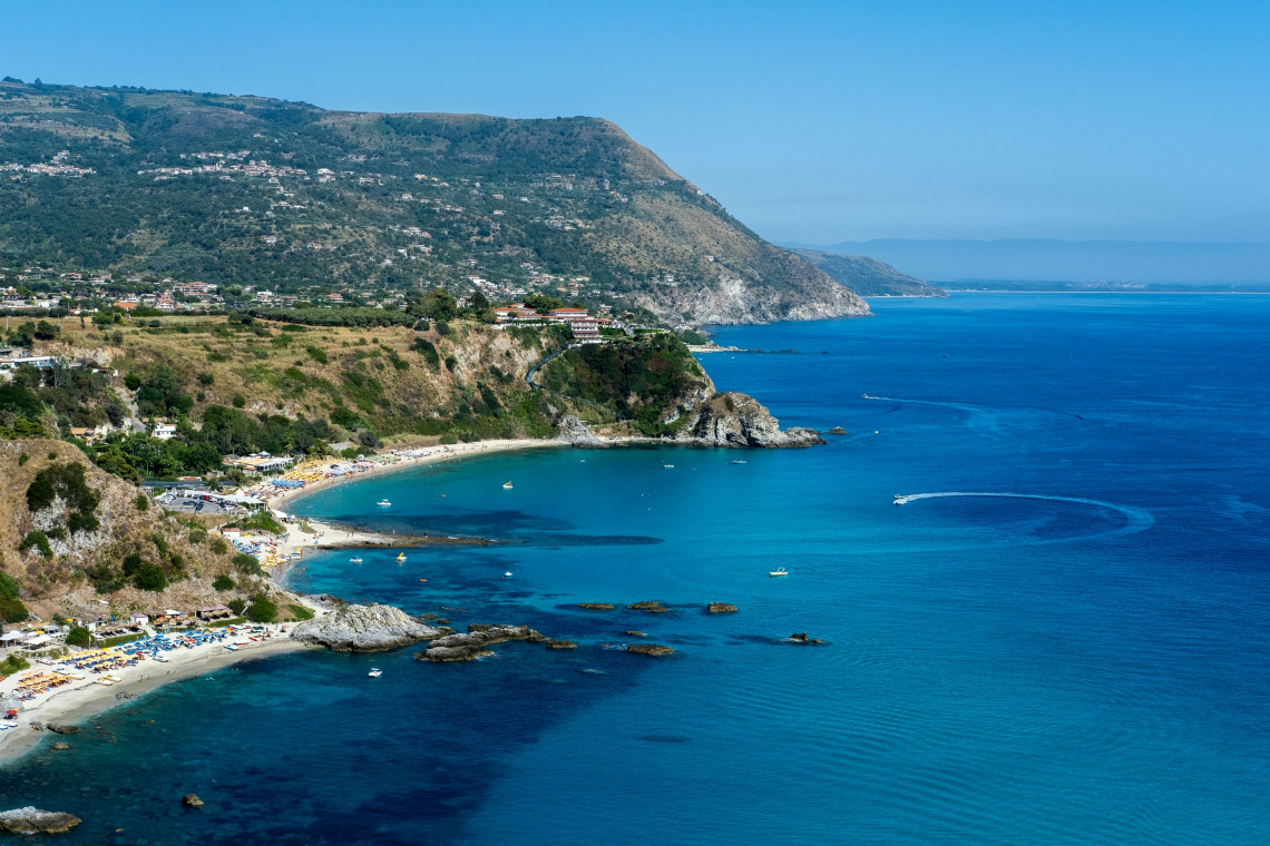 Aerial view of a sandy bay with turquoise water, beach umbrellas and green cliffs along the Calabrian coast, Southern Italy