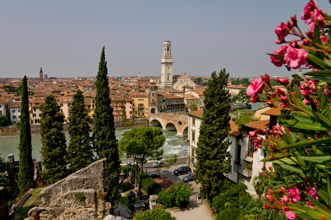 Panoramic view over Verona, Italy, with the Adige River, Ponte Pietra and the towers and terracotta rooftops of the historic centre framed by cypress trees.