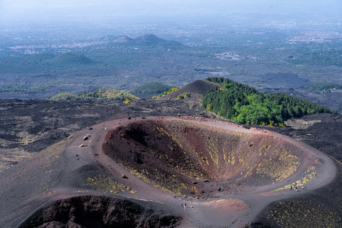 One of the Silvestri Craters on Mount Etna near Nicolosi, Sicily, with a walking trail circling the dark volcanic cone and extensive lava fields stretching toward the surrounding landscape.