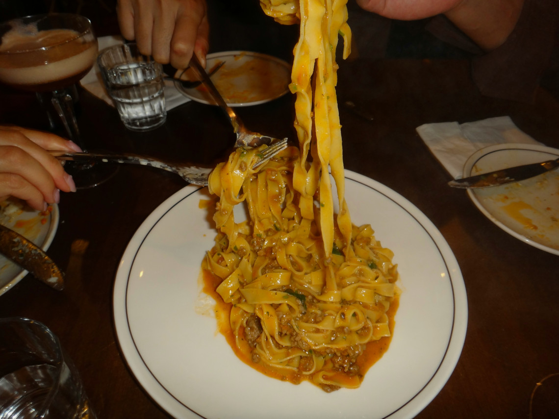  Fork lifting fresh tagliatelle pasta with meat rag&ugrave; sauce from a white plate at an Italian restaurant table