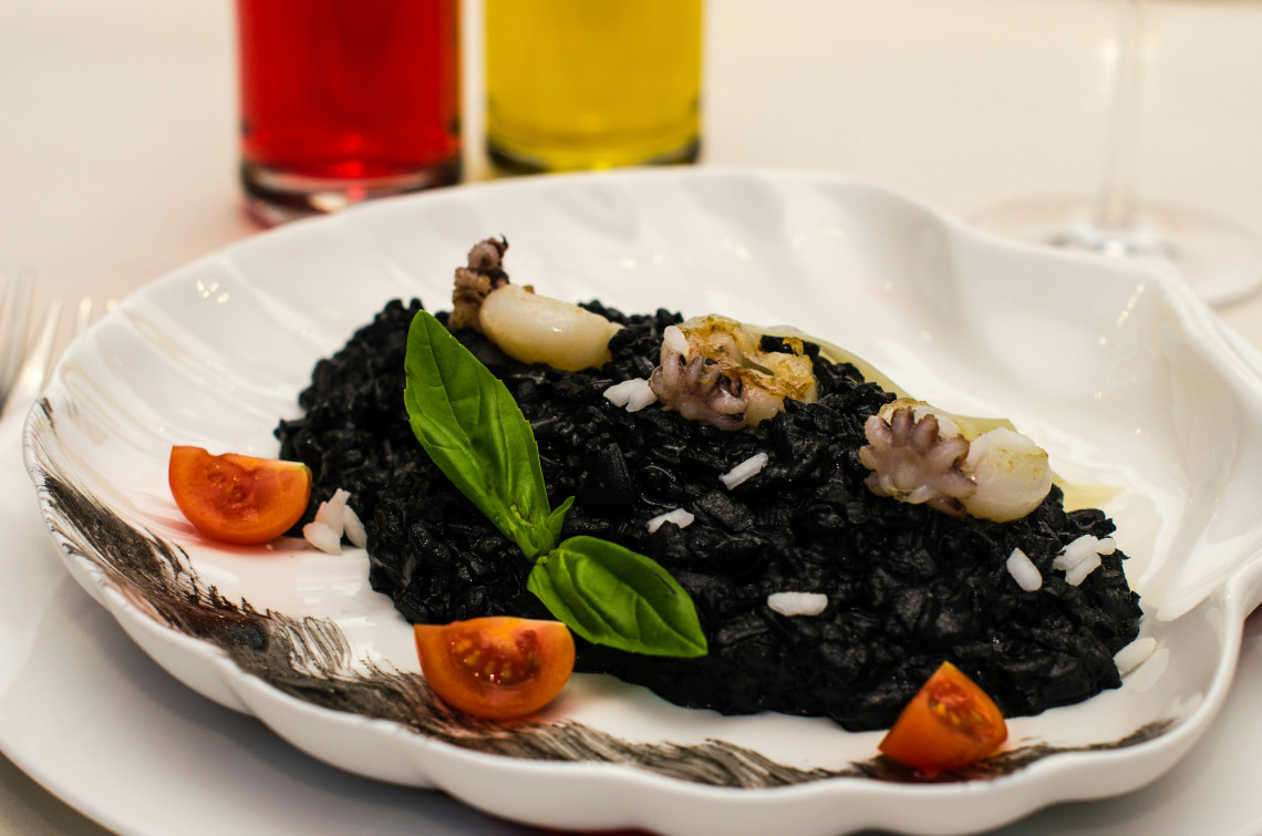  Plate of black squid ink risotto topped with baby octopus, cherry tomatoes and fresh basil, served at an Italian restaurant