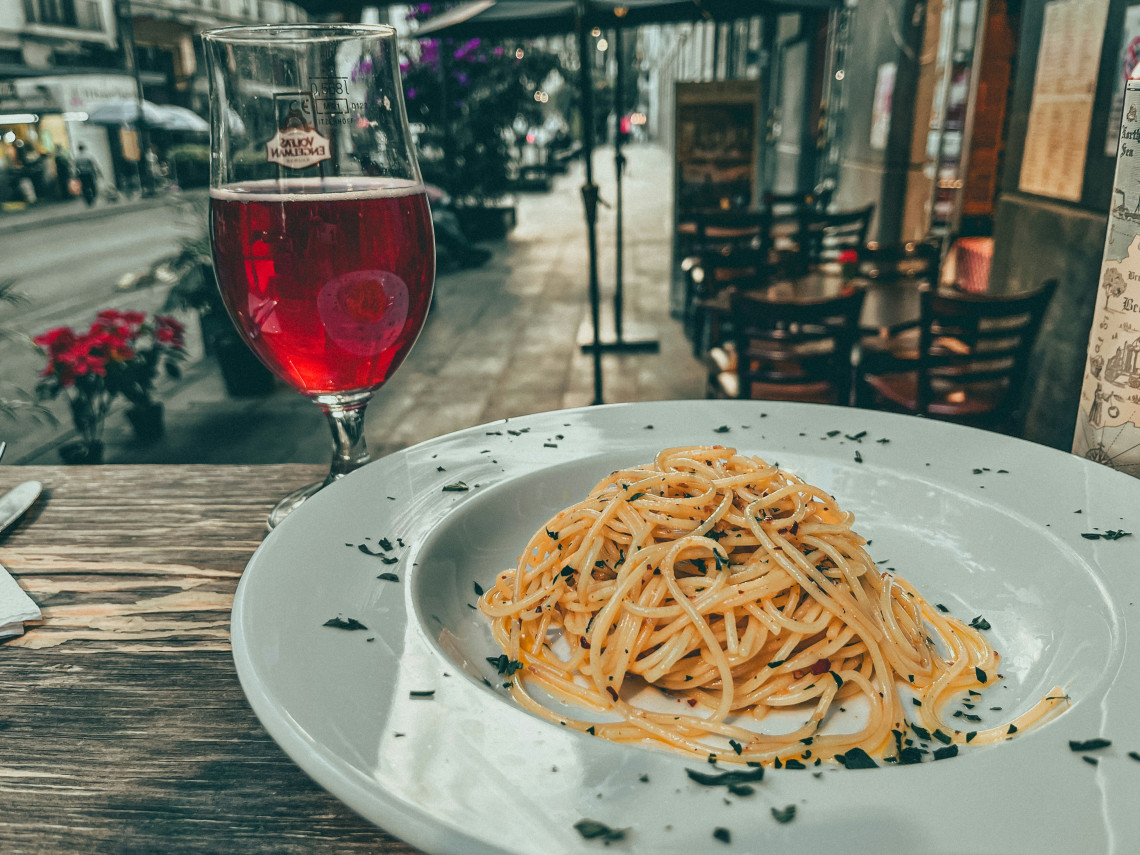 Plate of spaghetti aglio e olio with a glass of red wine on a wooden table at an outdoor Italian trattoria