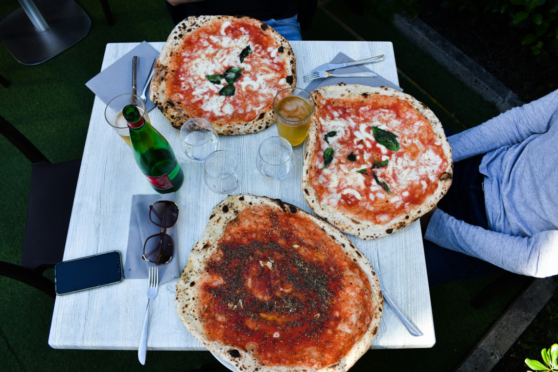 Three wood-fired Neapolitan pizzas margherita with charred crust, tomato sauce, mozzarella and fresh basil on an outdoor restaurant table in Italy