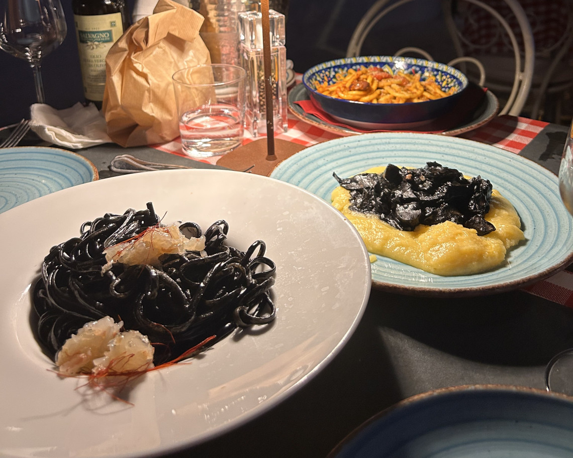 Table with squid ink spaghetti with shrimp, creamy polenta with cuttlefish, and tomato pasta at an Italian restaurant dinner