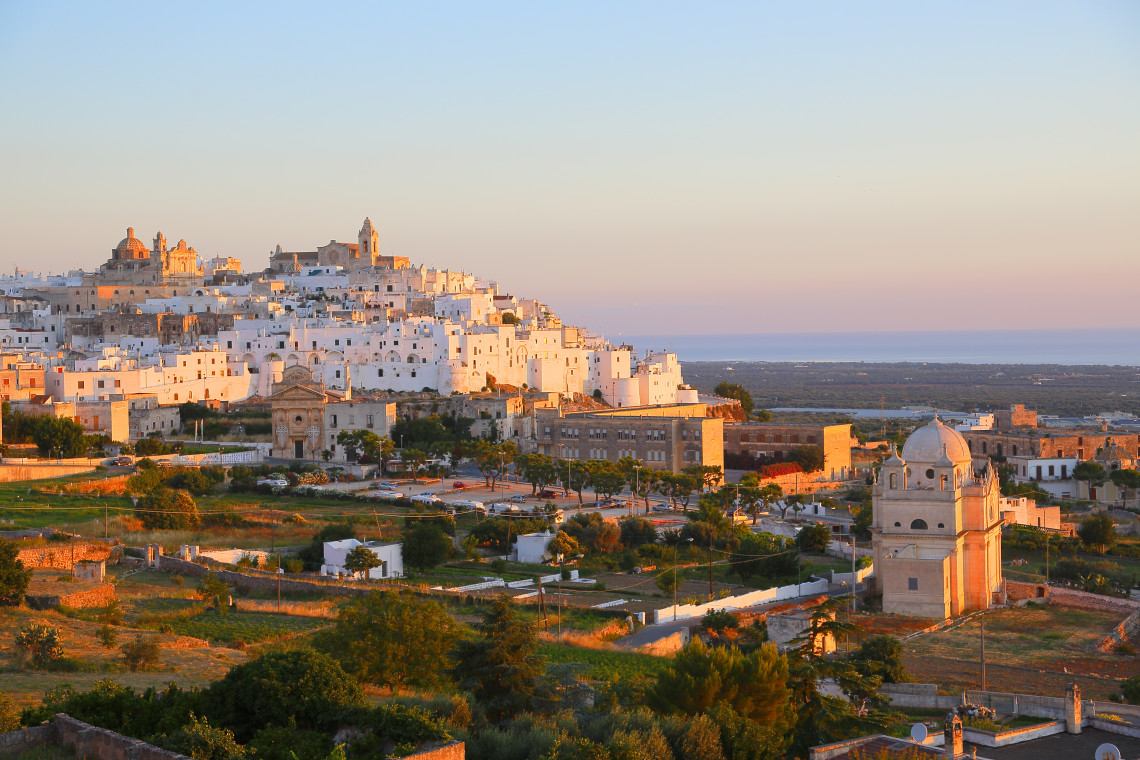 Panoramic view of Ostuni&rsquo;s historic centre in Puglia, with densely packed whitewashed buildings rising across the hillside in the warm evening light.