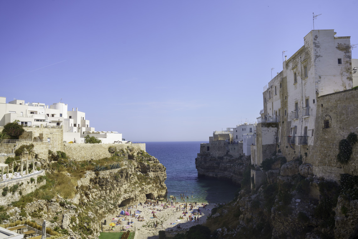 Lama Monachile beach in Polignano a Mare, Puglia, set in a narrow rocky cove between limestone cliffs topped with whitewashed buildings.