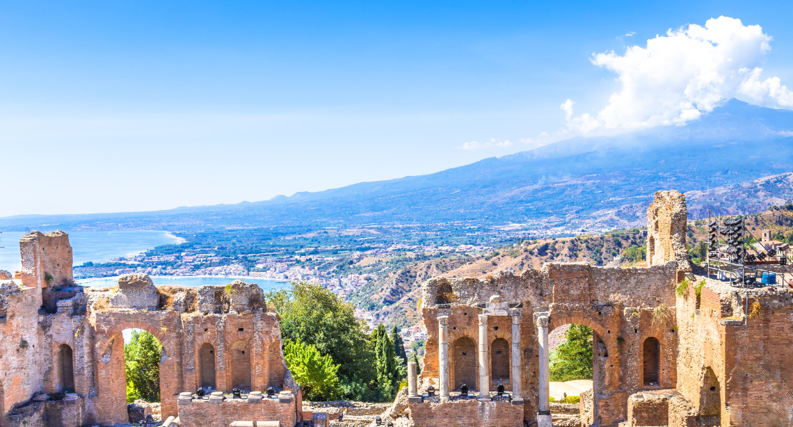 Ancient Greek theatre ruins in Taormina with arched brick walls framing a panoramic view of Mount Etna and the Ionian coastline, Sicily, Italy