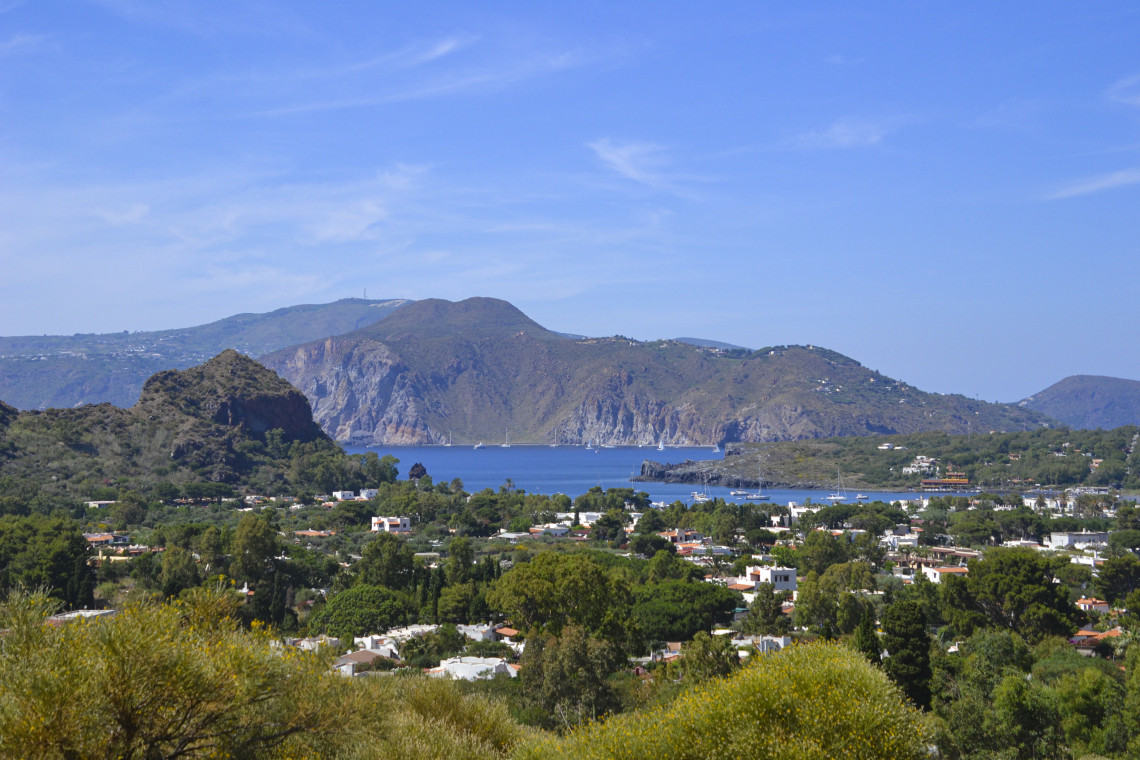 Panoramic view of Lipari town surrounded by lush Mediterranean vegetation with the volcanic crater bay and Tyrrhenian Sea in the background, Aeolian Islands, Sicily, Italy
