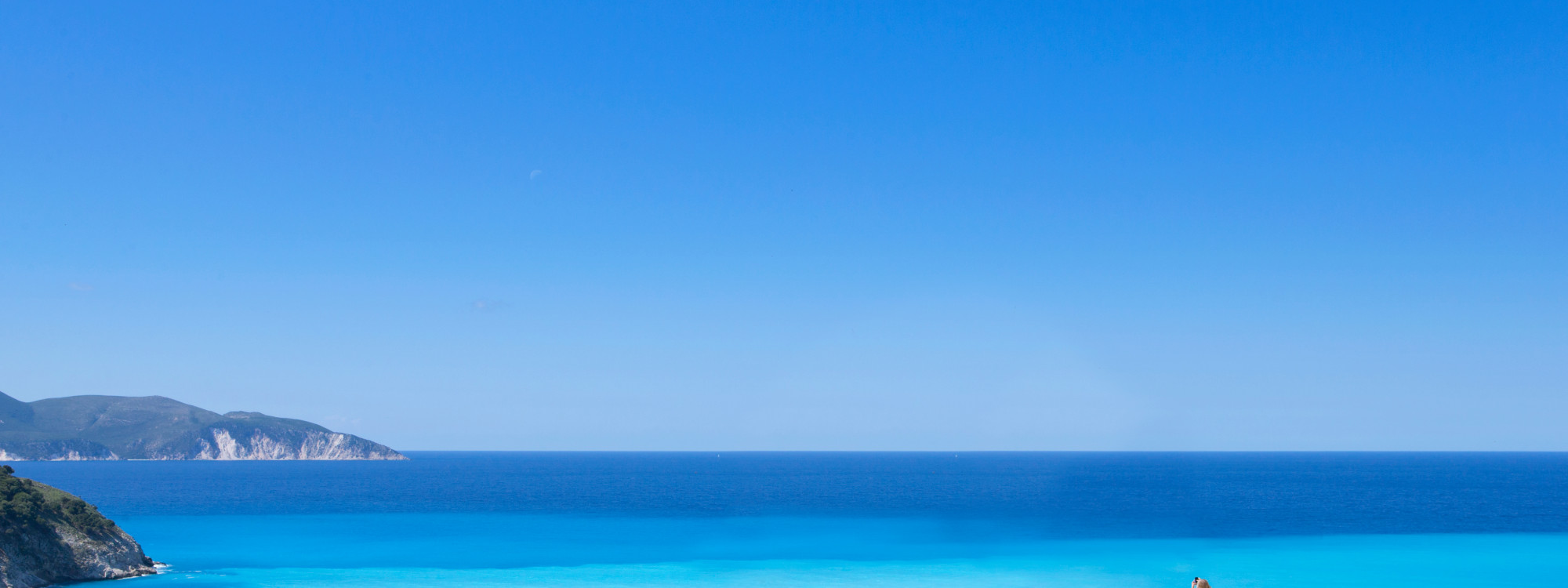 Panoramic view of vivid turquoise Mediterranean waters meeting a rocky coastline under a clear blue sky, Italy