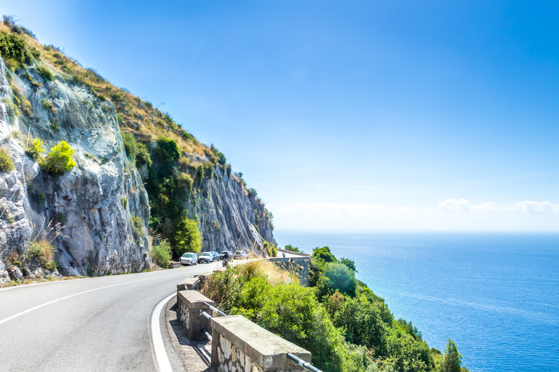 Winding SS163 Amalfitana coastal road carved into dramatic limestone cliffs with turquoise Mediterranean Sea views, Amalfi Coast, Campania, Italy