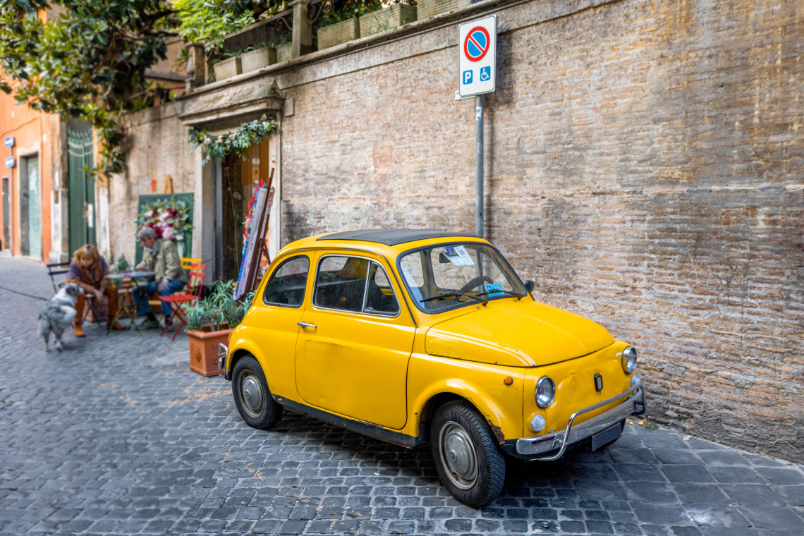 Vintage yellow Fiat 500 parked on a cobblestone street beside a brick wall in the Trastevere neighborhood, Rome, Italy