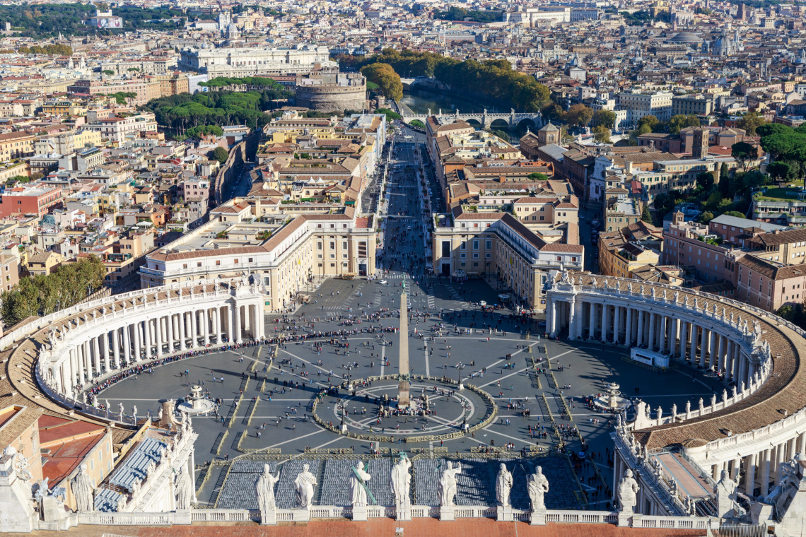 Elevated view from St. Peter&rsquo;s Basilica over St. Peter&rsquo;s Square in Vatican City. Bernini&rsquo;s curved colonnades surround the central obelisk, with Via della Conciliazione extending toward Rome.