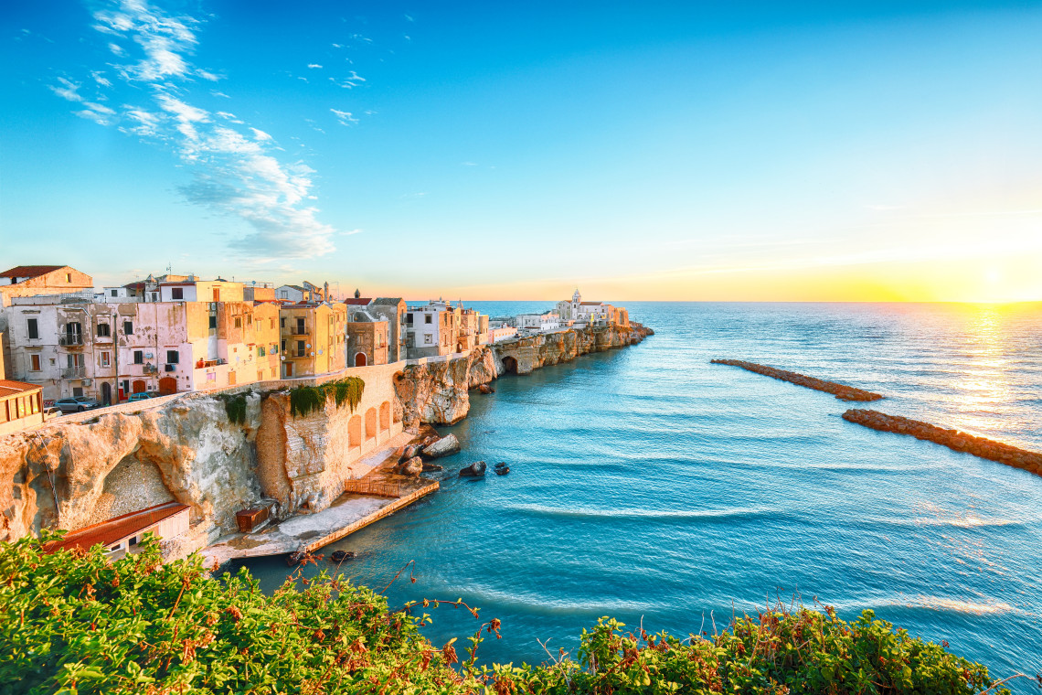 Panoramic sunset view of Vieste old town perched on limestone cliffs above the turquoise Adriatic Sea, Puglia, Southern Italy