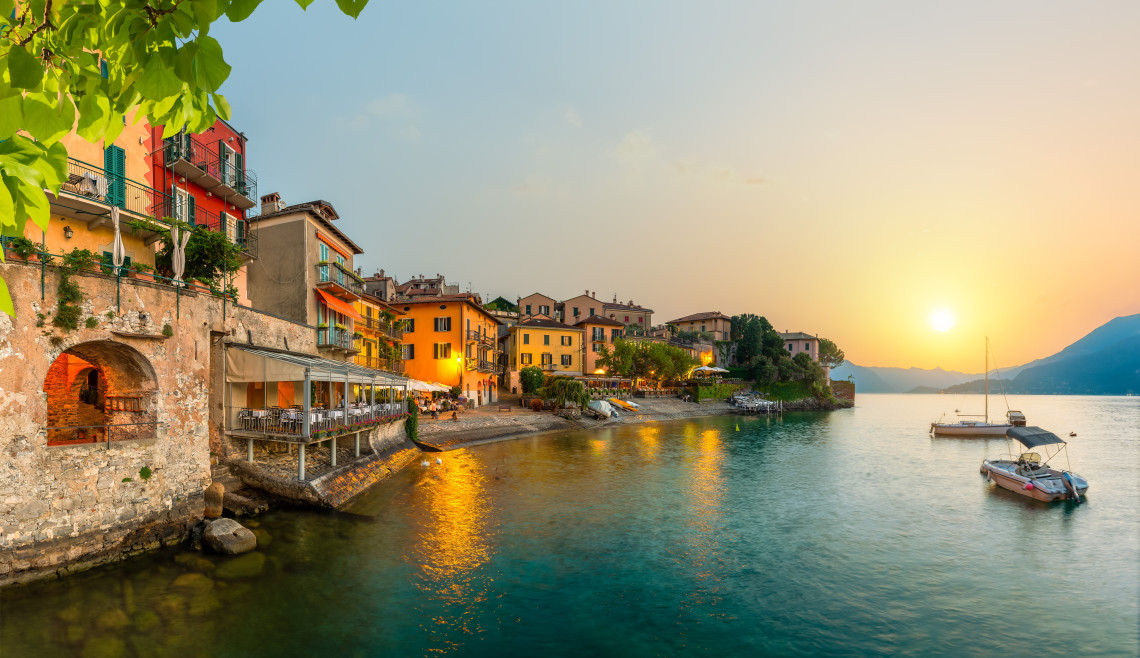 Panoramic sunset view of Varenna village with colorful buildings and lakeside restaurant reflected in the turquoise waters of Lake Como, Lombardy, Italy