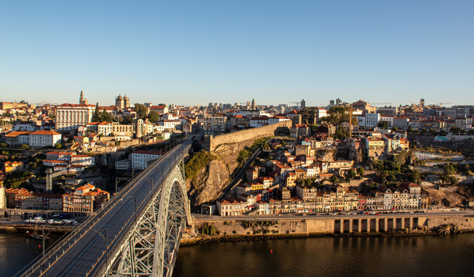 Panoramic view of Porto&rsquo;s riverside buildings and a large iron bridge crossing the Douro River under clear skies.
