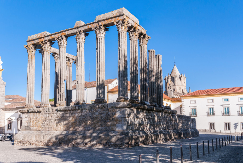 Ancient Roman Temple of &Eacute;vora with tall stone columns under a clear blue sky, surrounded by historic buildings in the old town.
