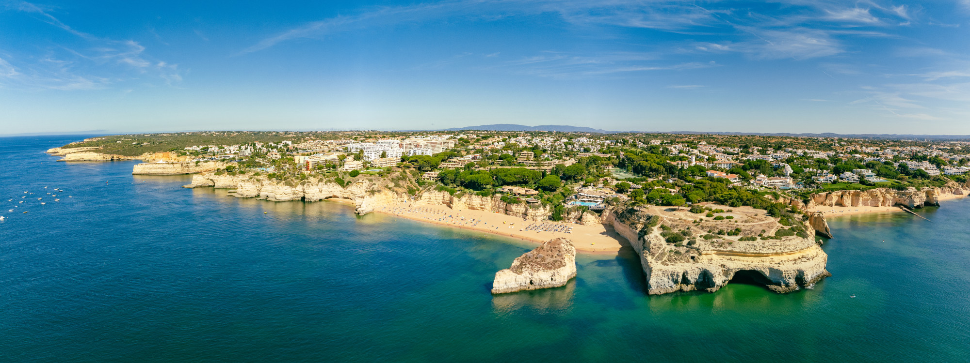 Aerial view of Praia da Marinha near Lagoa in the Algarve, Portugal, showing golden limestone cliffs, a sandy cove and natural rock arches surrounded by blue Atlantic water.