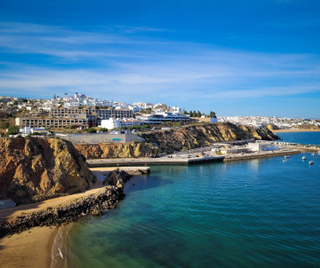 Praia da Baleeira sits within a sheltered bay near Albufeira Marina in the Algarve, Portugal. Golden cliffs, white buildings and clear Atlantic water shape the surrounding coastline.