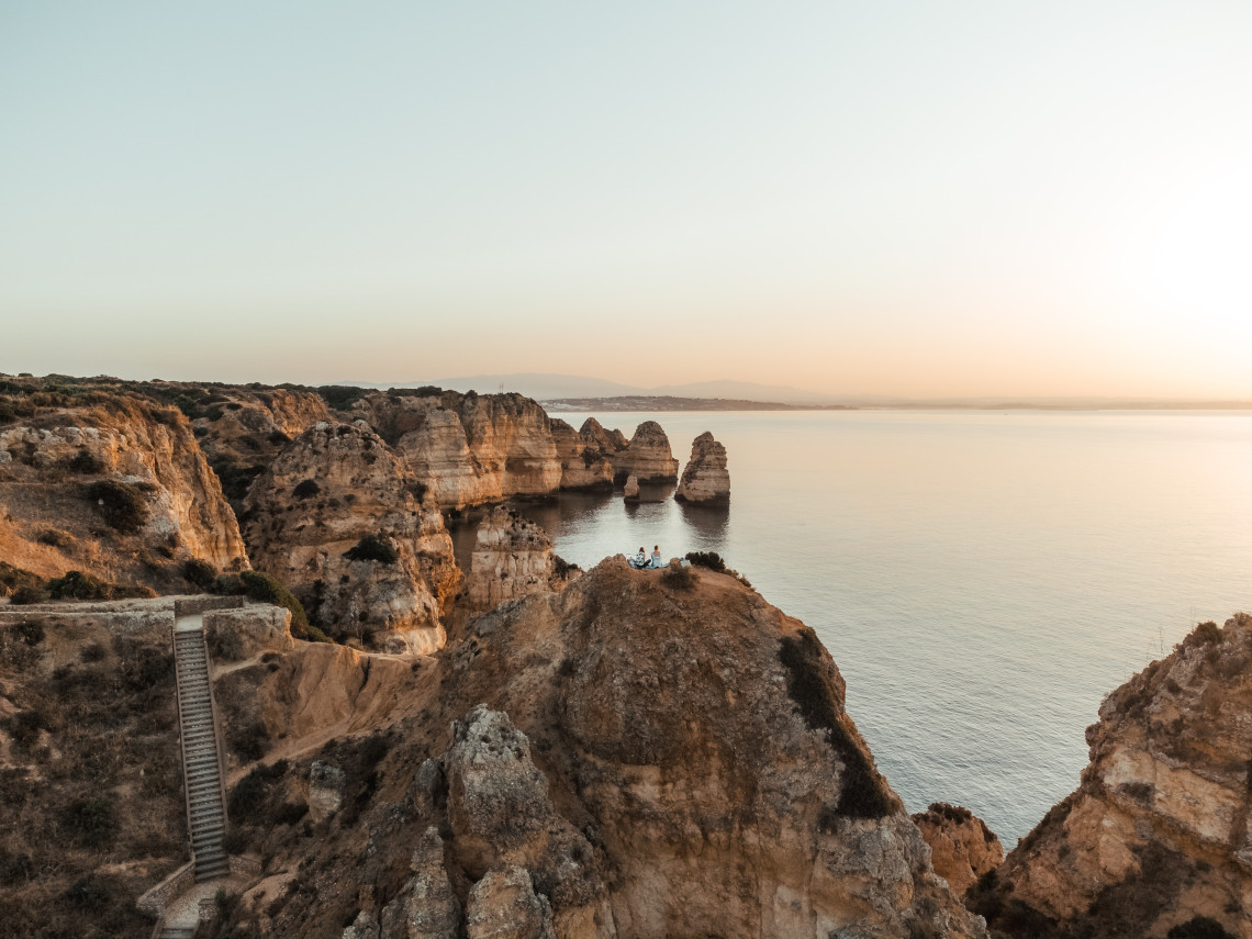 Coastal view of Ponta da Piedade in Lagos at golden hour, with dramatic limestone cliffs, sea stacks and calm Atlantic water extending toward the horizon.