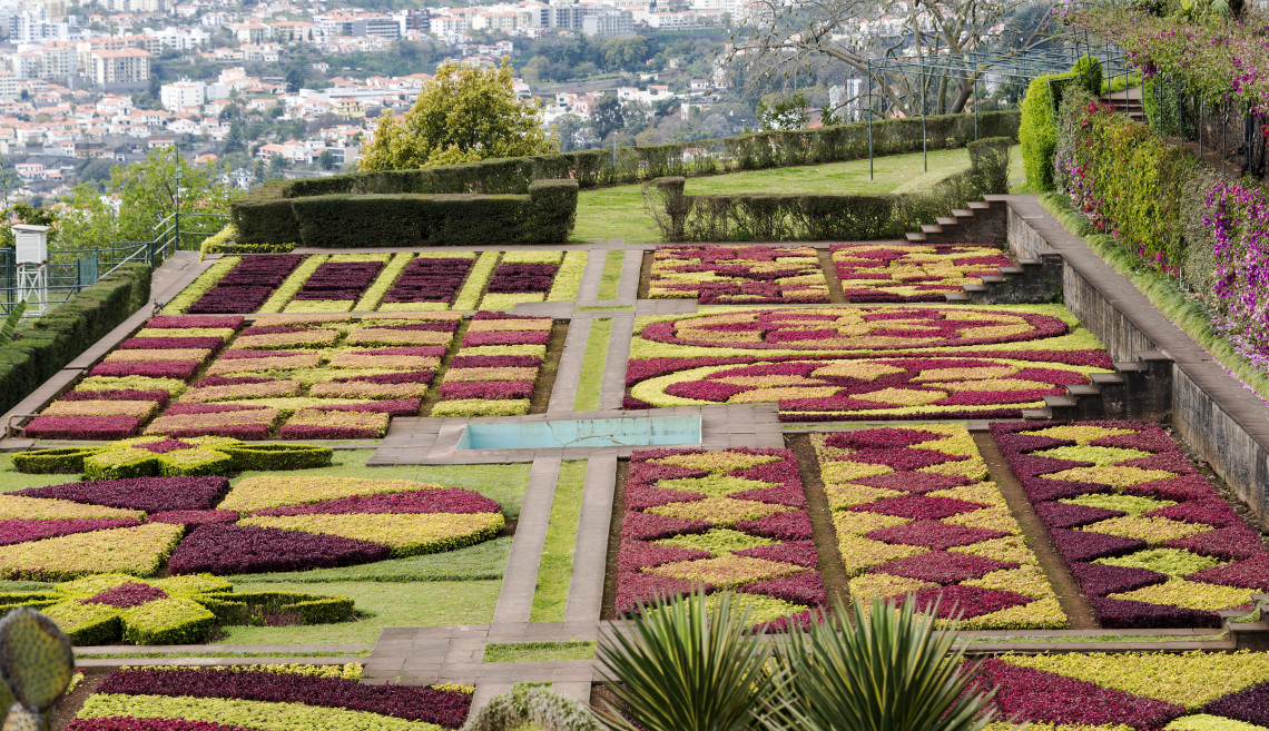 View of the Madeira Botanical Garden in Funchal, Madeira, Portugal, featuring geometric flower beds, manicured hedges, and ornamental landscaping overlooking the city. The garden is one of Madeira's most visited attractions, known for its diverse plant collections and panoramic views.