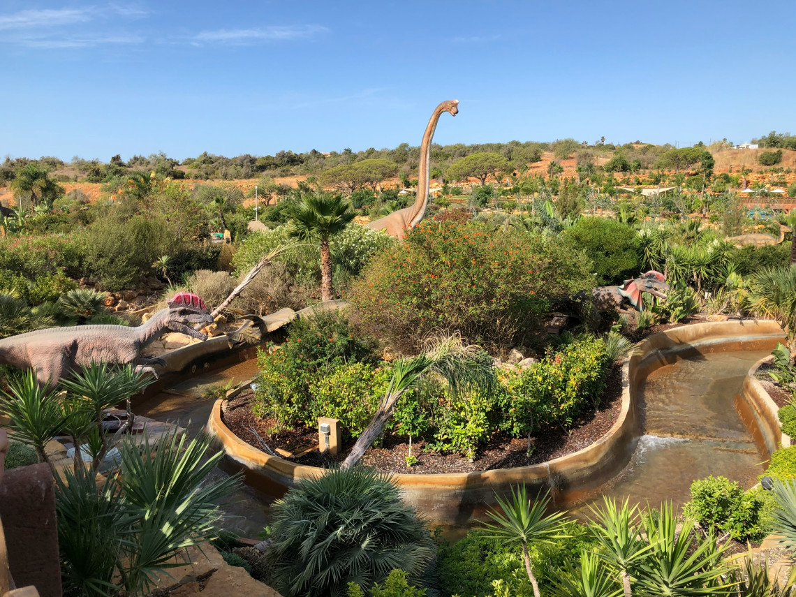 Large dinosaur models and themed attractions surrounded by landscaped vegetation at Zoomarine in Guia, Algarve, Portugal.