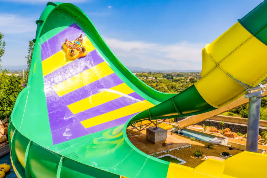 A large colorful water slide at Slide & Splash in Lagoa, Algarve, with visitors descending the attraction under a clear blue sky.