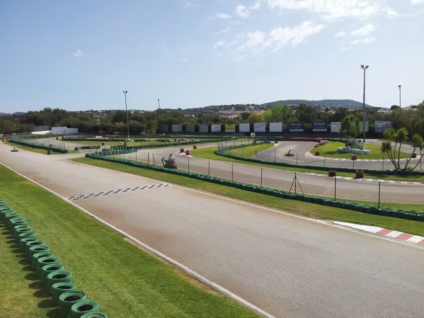 Go-karts race around the outdoor circuit at Karting Almancil in the Algarve, with safety barriers, landscaped track sections and a checkered finish line.