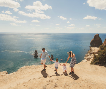 A family walks along the golden limestone cliffs of Ponta da Piedade in Lagos, overlooking the Atlantic Ocean and distinctive offshore rock formations.