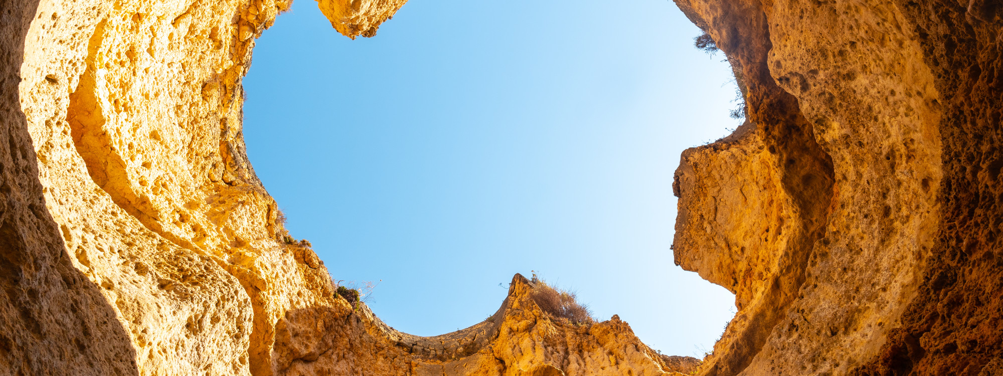 Interior view of Benagil Sea Cave in the Algarve, Portugal, looking upward through the natural skylight opening surrounded by golden limestone rock formations. The image showcases the distinctive geological features of one of the Algarve’s most visited se